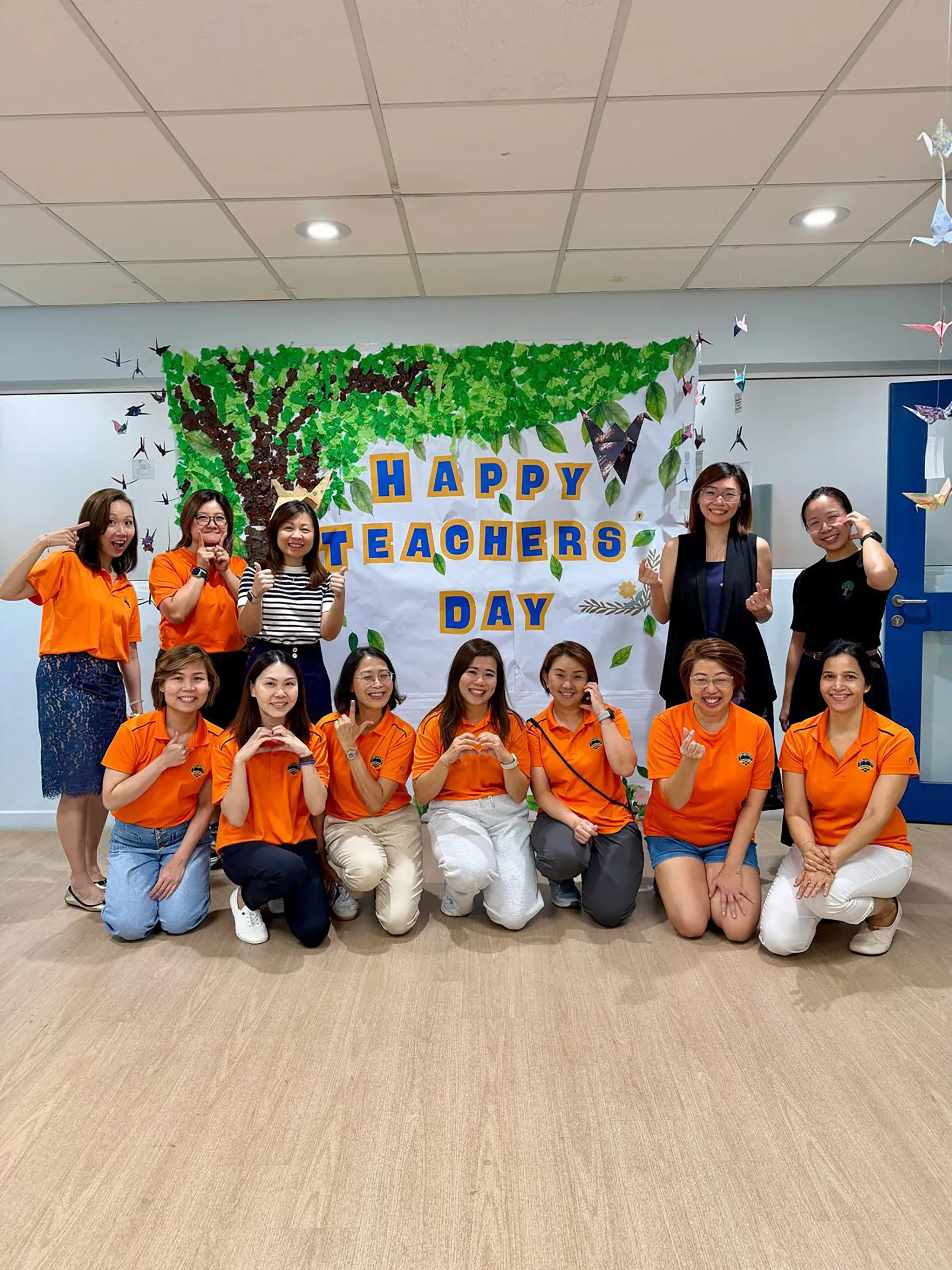Parent volunteers and our school leaders pose in front of a “Happy Teachers’ Day” display.